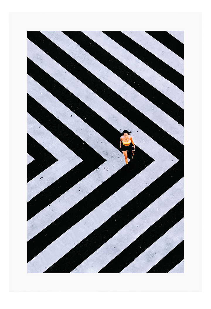 An urban wall art with an aerial view of a lady walking on black and white street crossing stripes